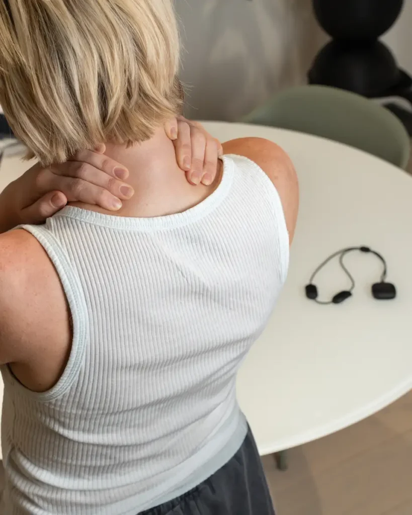 A woman experiencing neck tension with the Serenity Comfort neck massager on the table nearby, designed for targeted muscle relaxation.